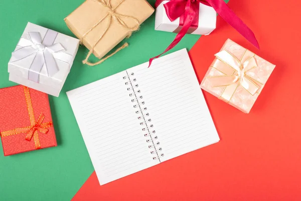 Weihnachtsgeschenkboxen, auf hellem Hintergrund mit offenem Schreibblock. Draufsicht, Urlaubs- und Weihnachtskonzept. — Stockfoto