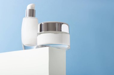 Podyumda kremalı kozmetik cam şişeler ve sert gölgeli yüz maskesi. Güzellik salonu ve doğal kozmetik ürünleri konsepti.