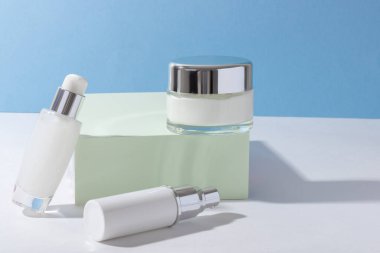 Podyumda kremalı kozmetik cam şişeler ve sert gölgeli yüz maskesi. Güzellik salonu ve doğal kozmetik ürünleri konsepti.