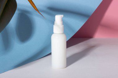 Açık mavi arka planda, sert gölgeli beyaz kozmetik şişesi. Güzellik salonu ve doğal kozmetik ürünleri konsepti.