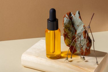 Üzerinde damlalık olan cam bir kozmetik şişesi, parlak güneş ışığında, ahşap bir kürsüde kurutulmuş bir çiçeğin yanında duruyor. Doğal kozmetik kavramı, doğal temel petrol..