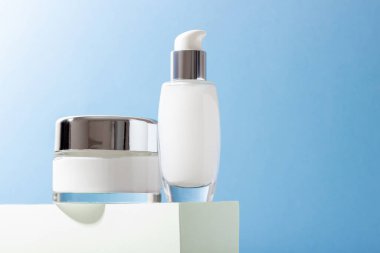 Podyumda kremalı kozmetik cam şişeler ve sert gölgeli yüz maskesi. Güzellik salonu ve doğal kozmetik ürünleri konsepti.