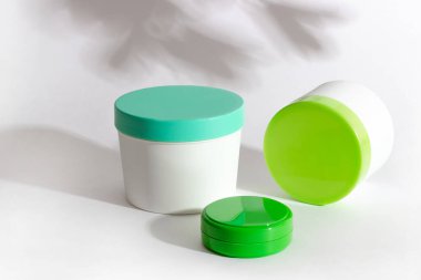 Beyaz arka planda kremalı ve maskeli tüpler ve sert gölgeler. Kozmetik ürünlerin kavanozları. Profesyonel cilt bakımı ve doğal kozmetik kavramı