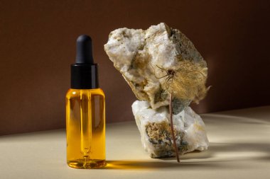 Bir cam kozmetik şişesi bir taşın yanında parlak güneş ışığında bej bir zemin üzerinde duruyor. Doğal kozmetik kavramı, doğal temel petrol..