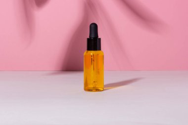 Arka planda gölgeler olan serum şişesi. Cilt bakım ürünleri ve pipette.