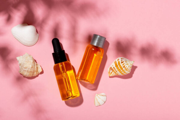 Tanning oil. Cosmetic products next to seashells in sunbeams on a pink background. Sun protective cosmetics.
