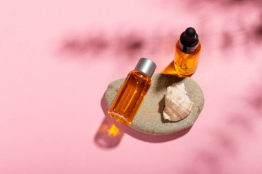 Bronzlaşma yağı. Kozmetik ürünleri deniz kabuklarının yanında pembe bir arka planda güneş ışınları içinde. Güneş koruyucu kozmetikler.