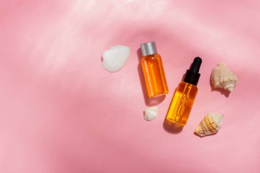 Bronzlaşma yağı. Kozmetik ürünleri deniz kabuklarının yanında pembe bir arka planda güneş ışınları içinde. Güneş koruyucu kozmetikler.