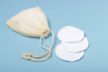 Pamuk çıkarılabilir makyaj pedleri bir bez torba içinde ve yüz yıkama ve temizleyici mavi arka planda. Ekoloji ve bilinçli tüketim kavramı. Yeniden kullanılabilir pamuk pedleri