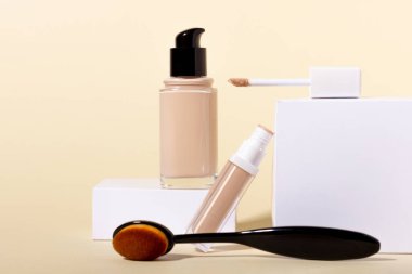 Makyaj fırçası ve kapatıcı şişedeki sıvı temel. Bej arkaplanda kopya alanı olan yüz düzeltici. Kopyalama alanı olan paketleme modeli