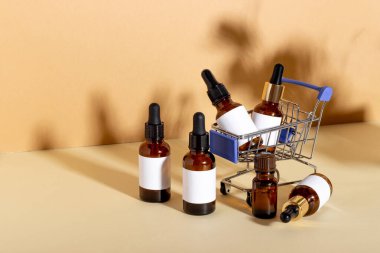 Bir alışveriş arabasında, gölgeli sarı bir arka planda yüz bakımı için bir damlası olan kozmetik ürünler. Kozmetik ürünleri alma, online alışveriş