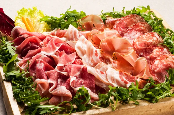 Salami cold cuts in box surrounded with greens — Stock Photo, Image