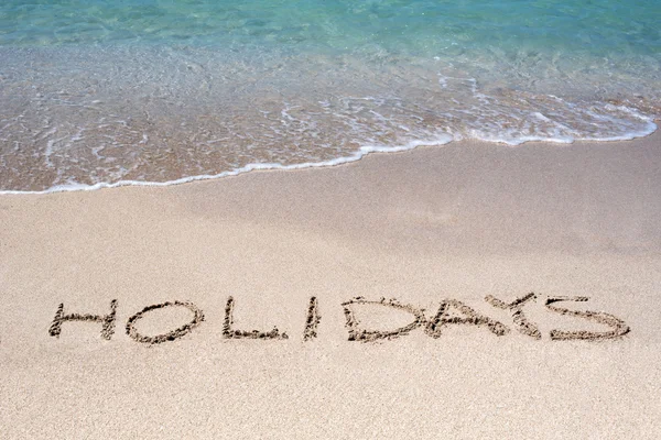 Word Holidays sketched on a tropical beach Royalty Free Stock Images