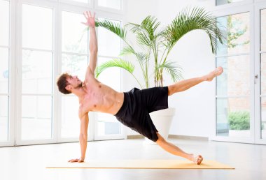 Vücut kaslarını, kol ve bileklerini güçlendirmek için yan kalas yogası yapan bir adam sağlık ve fitness konseptinde yüksek anahtarlı bir spor salonunda yan görünüşte.