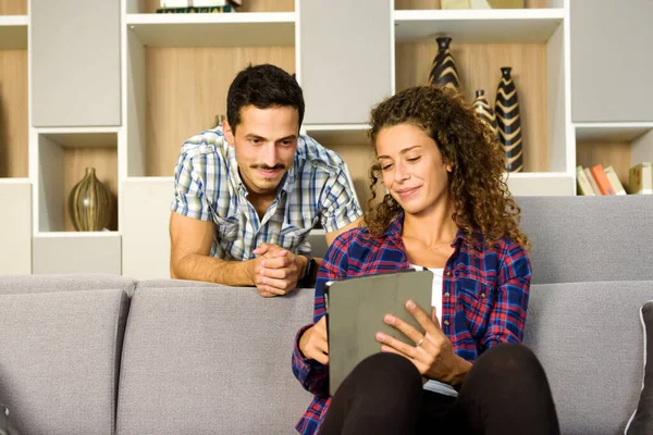 Genç bir çift, kişisel eğlence konseptiyle mutlu bir gülümsemeyle birlikte oturma odalarında oturup tablet-bilgisayarda medya yayınlıyor.