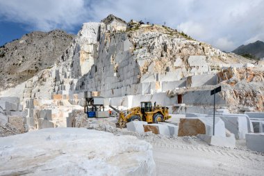 Carrara mermer ocağı, Toskana, İtalya 'da. Kesik taş blokları ve dağ zirvesinin altında ağır görev ekipmanları var.