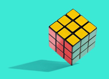 Renkli çözülmüş Rubiks Küpü kenarlarda dengelenmiş, belli bir rengin karelerini içeren bir yapboz oyunu küpün her iki tarafında, bir gölgeyle birlikte Cyan bir arkaplanda düzenlenecektir.