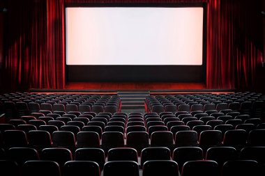 Boş bir sinema salonu ve sahnesi var. Arka koltukların arkasında kırmızı kadife perdeler var ve ekranda ışıklar var.