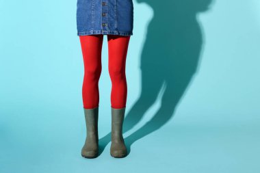 Yeşil lastik çizmeli genç bir kadın ya da kısa kot etek ve kırmızı külotlu çorap giyen ya da mavi arka planda poz veren ve daha düşük vücut görünümlü gölgeli bir kadın.
