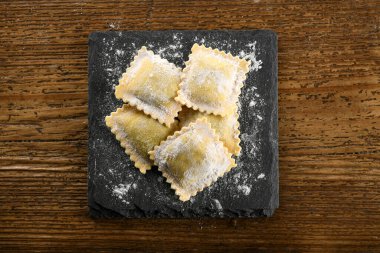 Tahtaya un serpiştirilmiş siyah tahta üzerine geleneksel İtalyan çiğ ravioli makarnasının üst görüntüsü.