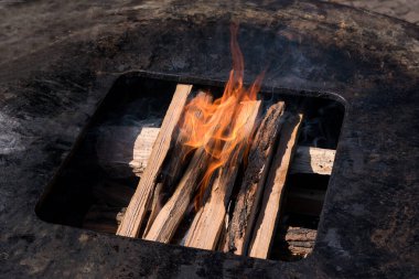 Mangal ateşinin kütükleri yüksek açılı bir açıdan yanmaya başlıyor. Sağlıklı bir yaşam tarzı ve yenilenebilir yakıt konseptiyle metal bir ızgaranın içinde.