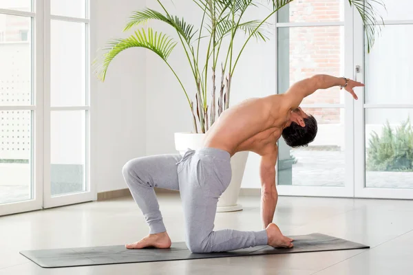 Man doing a backbend and twist yoga pose to increase mobility and flexibility of his body and muscles in a high key gym with copyspace in a health and fitness concept with copyspace