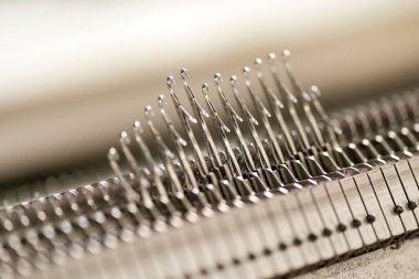 Latch needles raised on a commercial knitting machine in a knitwear factory with selective focus to one in the centre and copyspace in a production concept