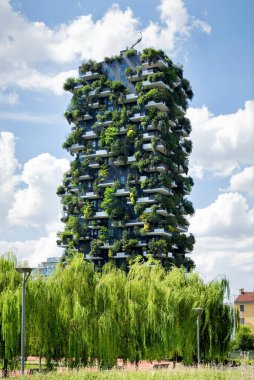 View of a Milan, Italy Vertical Forest apartment tower against blue sky with its terraces lined with leafy green trees in a metropolitan or urban reforestation project