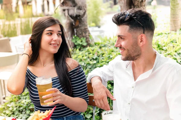 Attractive young woman flirting with a man over beers at an outdoor restaurant or pub as they enjoy a romantic date smiling into each others eyes