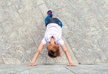 Atletik kadın şehrin kaldırımında esneme egzersizleri yapıyor. Bir binanın duvarına yaslanmış, spor konseptiyle kollarını açmış.