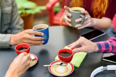 Kahve molası veren bir grup genç arkadaş ellerinde fincanlar ve kahve fincanlarıyla bir masanın etrafında oturuyorlar.