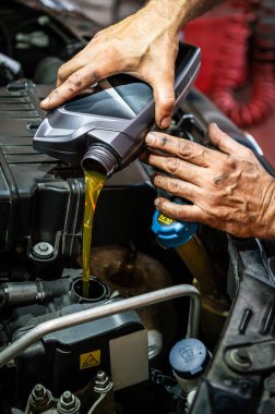 Tamirci elleri bakım için araba motoruna taze motor yağı döküyor.