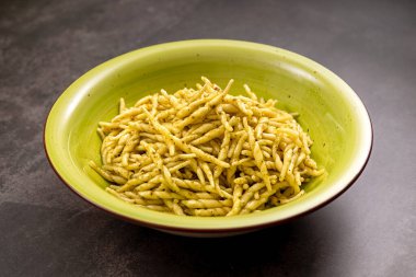 Açık yeşil bir kâsede yeşil pesto soslu trofie makarna İtalyan mutfak geleneğini temsil ediyor.