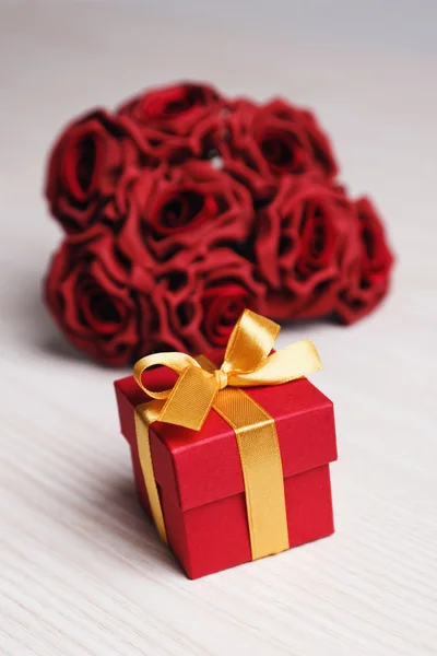 Red flowers and gift box with yellow ribbon — Stock Photo, Image