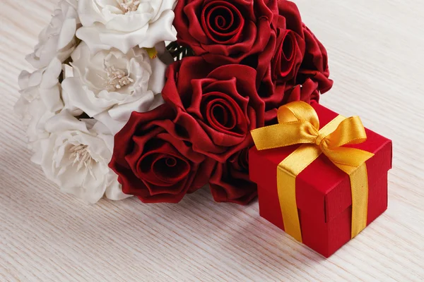 Червоні квіти і подарункова коробка з жовтою стрічкою — стокове фото