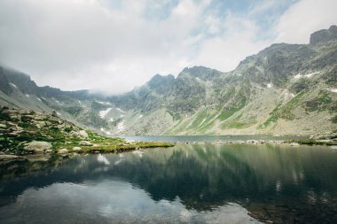 Dağlar arasında Hincovo pleso. Sisteki dağların arka planına karşı kristal berrak göl manzarası. İnanılmaz bir manzara..