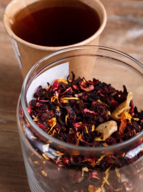 Bir bardak Karkade çayı ve tek kullanımlık kağıt bardakta demlenmiş çay, ahşap kırsal arka planda. Üst görünüm.