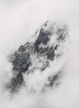 Beyaz bir bulut örtüsüyle çevrili engebeli kayalık dağların mistik fotoğrafı.