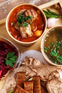 Ukrayna 'nın geleneksel borş çorbası ve kağıt bardaklarda sebze çorbası cam kasede pancar salatası ekmek kırıntıları ve rustik ahşap tepside yeşil soğan. Ukrayna yemekleri. Ukrayna menüsü.