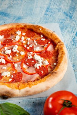 Salamlı, jambonlu, biberli ve süzme peynirli çıtır pizza. Pizza mavi arka planda yatıyor..