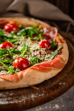 Arugula, prosciutto ve ahşap bir tahtanın üzerinde kiraz domatesli pizza. Menü için fotoğraf.