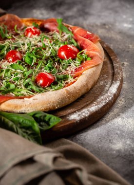 Arugula, prosciutto ve ahşap bir tahtanın üzerinde kiraz domatesli pizza. Menü için fotoğraf.