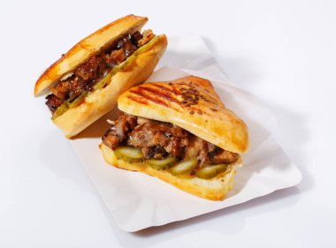 Tek kullanımlık kağıt tabakta etli ve salatalık turşulu sıcak sandviç. Beyaz arka plan. Yan görünüm.