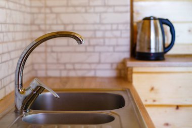 Küçük paslanmaz çelik bir musluğu kapat ve evdeki mutfağa batır. Mermer kiremitleri ve ahşap mobilyaları olan parlak bir mutfağın ayrıntıları. Bulanık arkaplan.