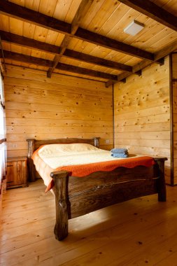 Rest in the mountains. Bright minimalist bright bedroom with wooden furniture and walls in a newly built mountain cottage. Handmade bed with a blanket and towels and a bedside table by the window.