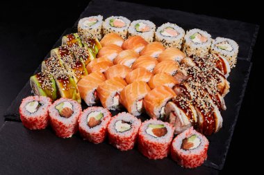 Siyah bir taşın üzerinde farklı dolgularla farklı suşiler. Lezzetli geleneksel Japon mutfağı, lezzetli deniz ürünleri ve restoran menüsü kavramı. Gıda arkaplanı.