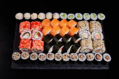 Siyah arka planda somon, sebze, balık, avokado, havyar ve susam tohumlu büyük bir suşi seti. Restoran menüsü.