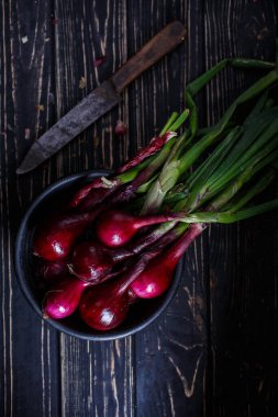 Tahta bir masada taze kırmızı soğan. Eski model bir bıçak. Taze sebzelerin atmosferik fotoğrafı.