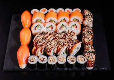 Japon suşi seti. Siyah arka planda taş bir tabakta farklı türde iştah açıcı dürümler. Üst manzara, düz uzanma.