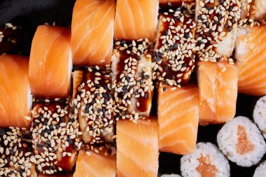 Philadelphia suşi rulolarının ve soslu sashimi rulolarının ve susam tohumlarının üst görüntüsü. Suşi rulolarının yaratıcı sunumu kavramı.